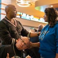 Two event attendees shaking hands while gentleman sitting at table in front of them makes a funny face for camera
